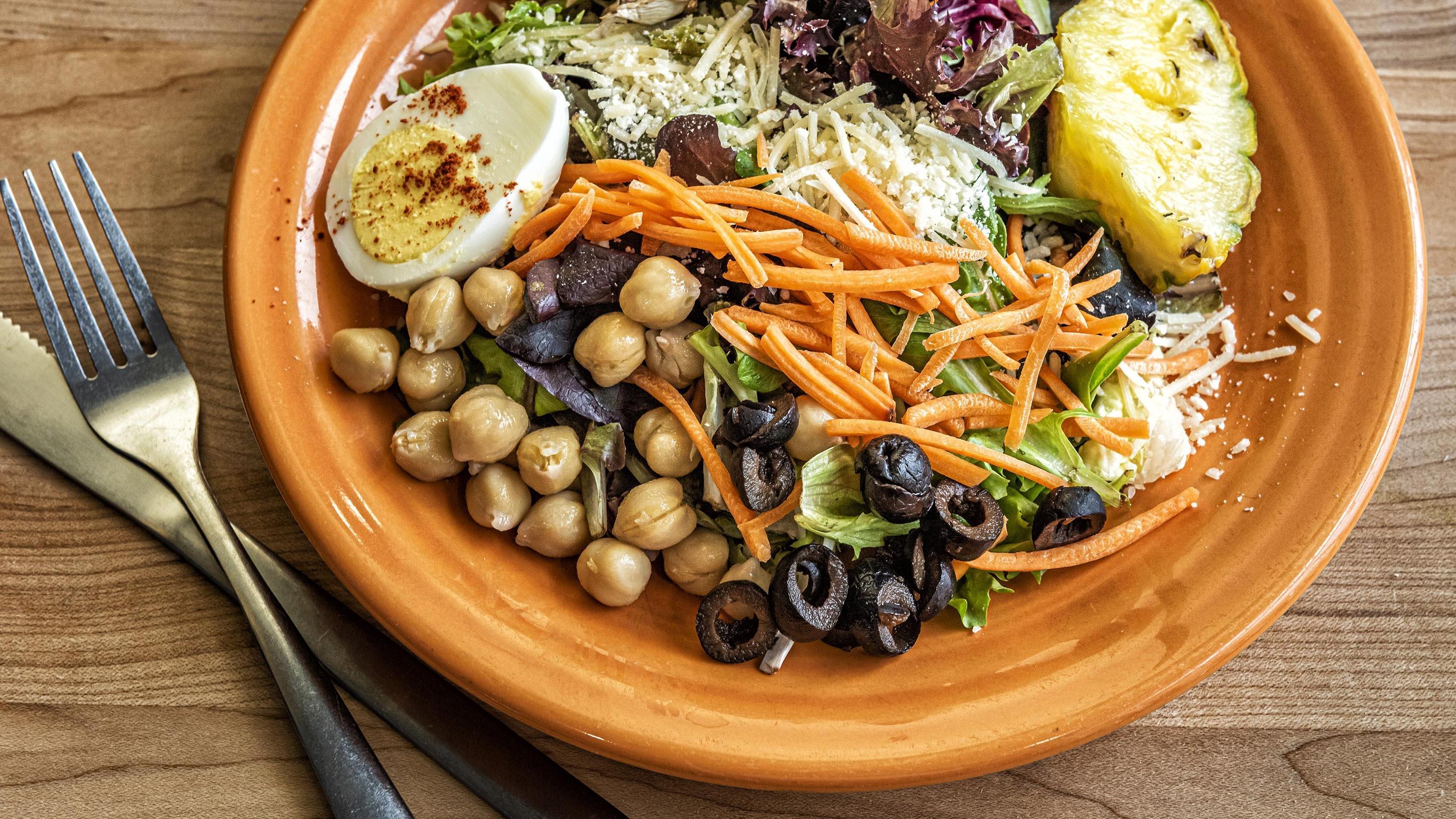 Salad, shredded carrots, black olives, and hard-boiled eggs on an orange plate in the Crow’s Nest Campus Restaurant.